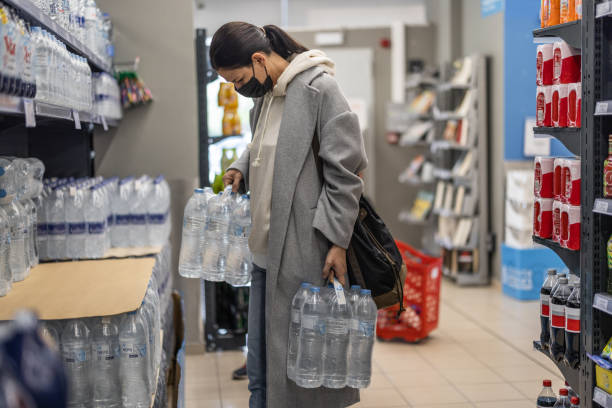 Woman with face mask picking plastic water bottles from shelf stock photo