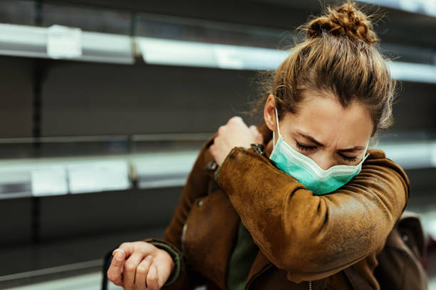 Woman with face mask sneezing into elbow while shopping in grocery store. Sick woman buying in supermarket and coughing into elbow during COVID-19 pandemic. cough stock pictures, royalty-free photos & images