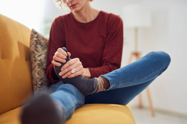 Woman with feet intense pain sitting on a couch at home. stock photo