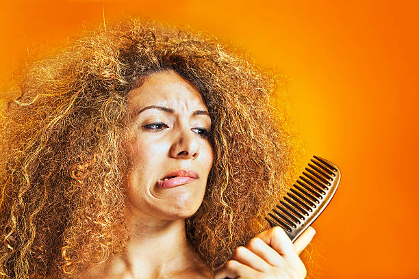 Woman with frizzy and curly hair looking at a comb Women with messy hair looking at her hairbrush. extremely matted hair stock pictures, royalty-free photos & images