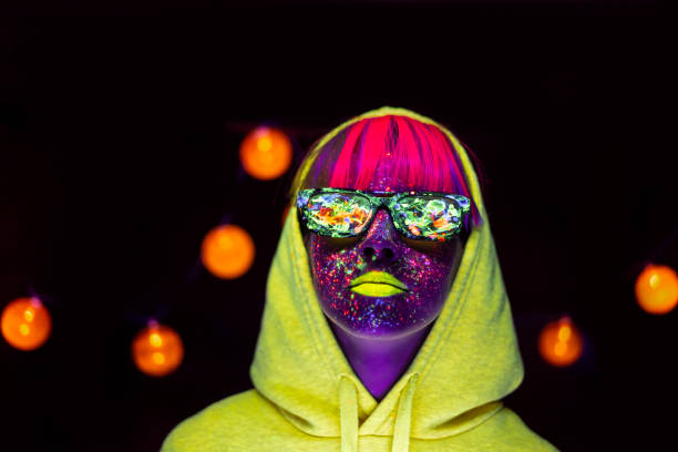 Woman with glowing makeup and sunglasses in black light Woman with neon makeup powder on face in studio. Young woman painted with fluorescent make up. paint neon color neon light ultraviolet light stock pictures, royalty-free photos & images