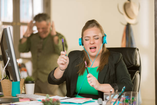 Woman with Headphones Singing Loudly and Annoying Colleague Young professional woman singing loudly enough to annoy a colleague arrogance stock pictures, royalty-free photos & images