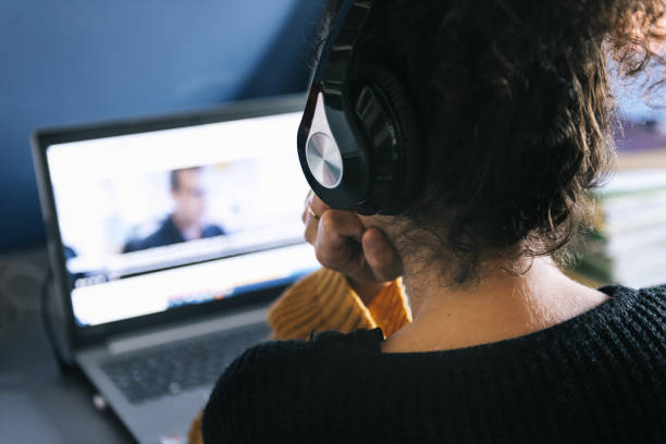 woman with headphones watching a movie on laptop rear view of a woman with headphones watching a movie on laptop at home, technology and entertainment concept, selective focus spectator stock pictures, royalty-free photos & images