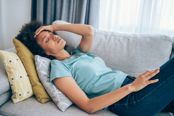 Woman with high fever at home. Sick young woman lying on the couch and holding her head with hand. Ill woman lying on the sofa with high temperature. tired stock pictures, royalty-free photos & images