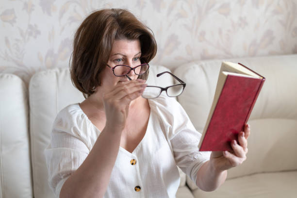 Woman with impaired vision reading a book through two glasses stock photo