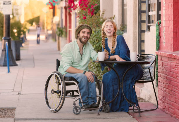woman with man in wheelchair at cafe table - wheelchair street happy imagens e fotografias de stock