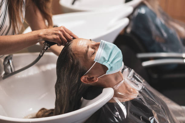 woman with mask getting her hairs washed in hair salon woman hairdresser coiffeur washing female clients hairs in times of coronavirus,  woman with eyes closed and mask relaxing, shallow focus hair salon mask stock pictures, royalty-free photos & images