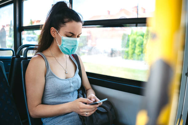 Woman with mask in bus Young caucasian beautiful woman with medical mask taking a bus ride and using her phone while riding. commercial land vehicle stock pictures, royalty-free photos & images