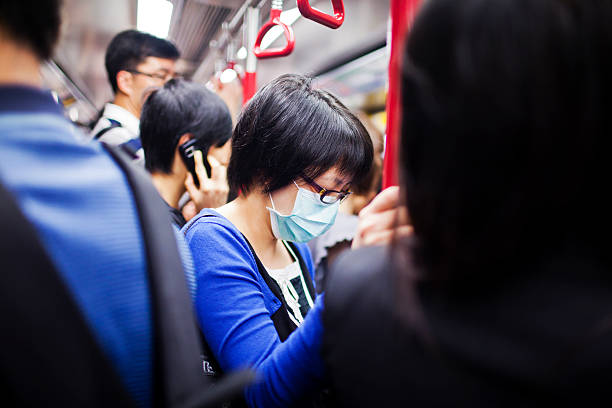 Woman with mask in subway train Hong Kong, China - September 27, 2011: Woman with mask among other passengers in subway train in Hong Kong. In 1997 the Avian influenza or bird flu virus H5N1 was discovered in Hong Kong from an human patient.  Concern raised dramatically when the mortaly rate was 30٪​ of the first 18 cases. Millions of poultry were killed to stop the disease. The population is still very cautious nowadays. aluxum stock pictures, royalty-free photos & images