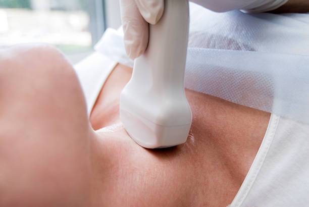 Woman with neck being scanned with ultrasound stock photo