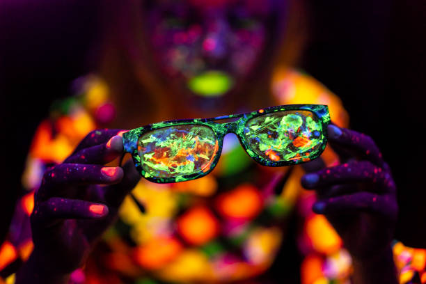 Woman with neon makeup powder on face holding colored sunglasses Woman with neon makeup powder on face in studio. Young woman painted with fluorescent make up. paint neon color neon light ultraviolet light stock pictures, royalty-free photos & images