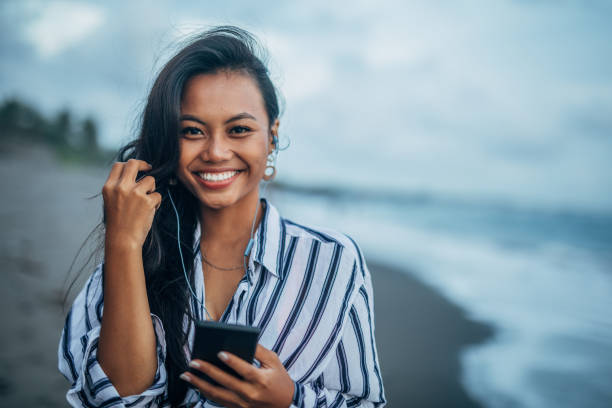Woman with phone and earphones at the beach Young woman with phone and earphones at the beach indonesian woman stock pictures, royalty-free photos & images
