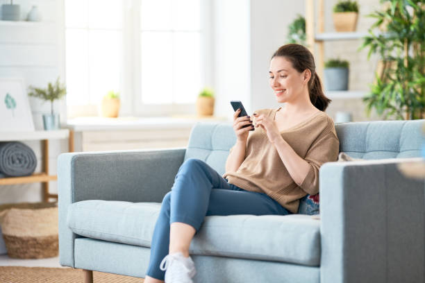 woman with phone Happy casual beautiful woman is talking on a phone sitting on a sofa at home. online shopping photos stock pictures, royalty-free photos & images