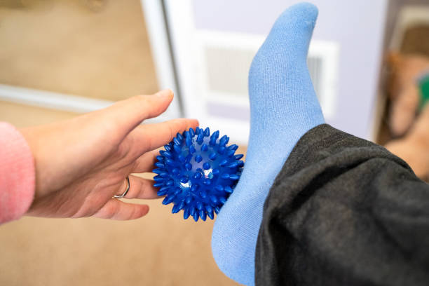 Woman with plantar fasciitis uses a spiky ball to massage her aching footu Woman with plantar fasciitis uses a spiky ball to massage her aching foot plantar fasciitis stock pictures, royalty-free photos & images