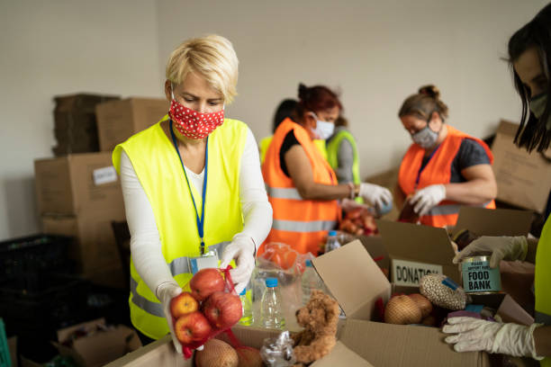 Woman with protective face mask helping collecting food in a homeless shelter Female volunteer collecting food for donation in a homeless shelter food bank stock pictures, royalty-free photos & images