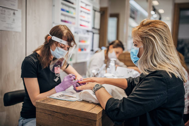 Woman with protective face mask on manicure treatment in beauty salon Beautician with face shield and mask giving manicure to female customer at beauty salon. Female customer also wearing face mask. Coronavirus control. painting fingernails stock pictures, royalty-free photos & images