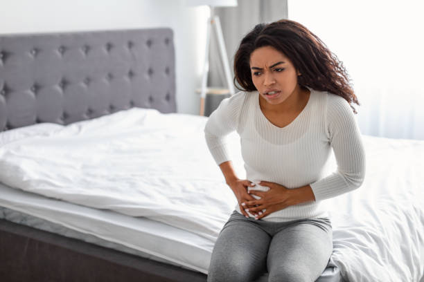 Woman with right side pain sitting on bed at home stock photo
