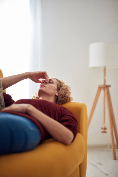 Woman with sinus pain, headache and stomach problems, lying on a couch at home. stock photo