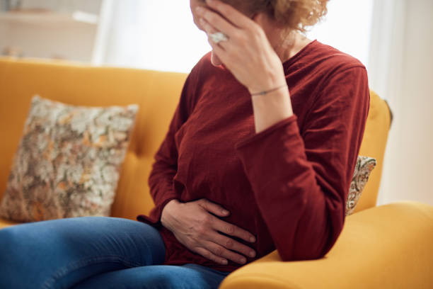 Woman with stomach pain and headache problem sitting on a couch at home. stock photo