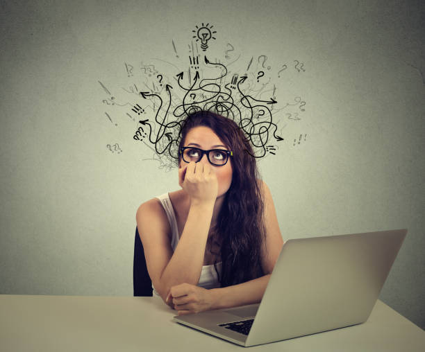 woman with thoughtful expression sitting at a desk with laptop with lines arrows and symbols coming out of her head Young woman with thoughtful expression sitting at a desk with laptop with lines arrows and symbols coming out of her head wasting time stock pictures, royalty-free photos & images