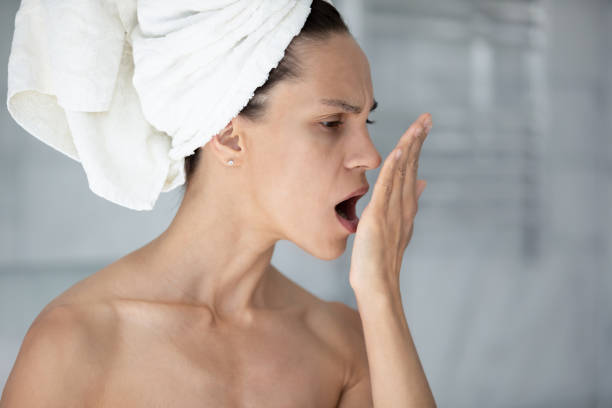 Woman with towel on head opens mouth check breath Woman with towel on head put palm in front face opens mouth check breath close up image. Suffers from unpleasant odor due to oral infections, poor dental hygiene, health problems, halitosis concept bad breath stock pictures, royalty-free photos & images