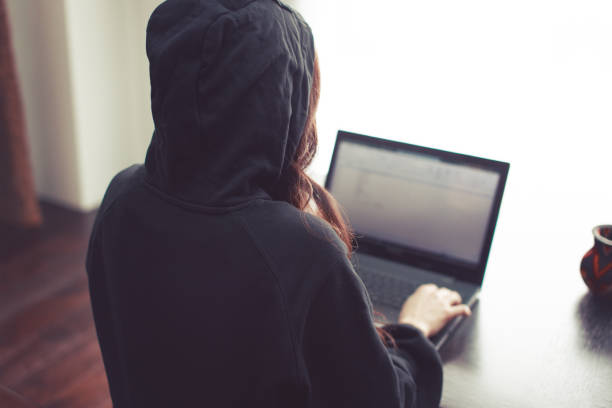 Woman working on laptop in hoodie at home from back view stock photo