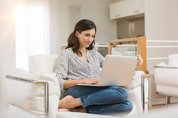 Woman working on laptop Young woman doing research work for her business. Smiling woman sitting on sofa relaxing while browsing online shopping website. Happy girl browsing through the internet during free time at home. correspondence photos stock pictures, royalty-free photos & images