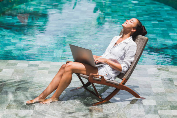 Woman working with laptop by the pool. Freelance work in tropical country stock photo