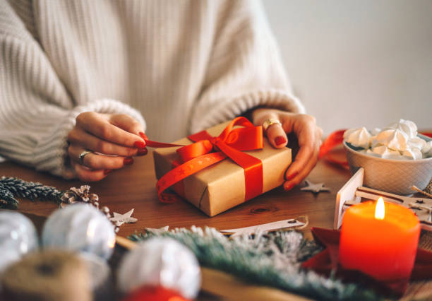 woman wrapping christmas presents at home - woman holding a christmas gift imagens e fotografias de stock
