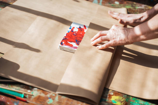 Woman wrapping her drawing at the paper while making present for somebody stock photo