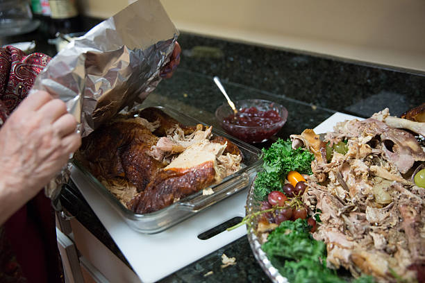 Woman wraps up leftover turkey from Thanksgiving dinner Caucasian woman whose face isn't visible is covering a glass pan of turkey leftovers with tin foil. The platter the turkey was on is beside it with the carcass and bits of turkey on it. They are sitting on a granite kitchen counter. Taken with a Canon 5D Mark 3. leftovers stock pictures, royalty-free photos & images