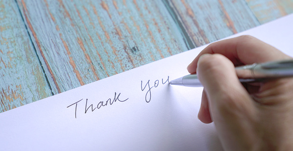 Woman writing thank you on card or paper. Close up view.