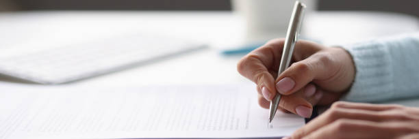 Woman writing with ballpoint pen in documents at table at home closeup stock photo