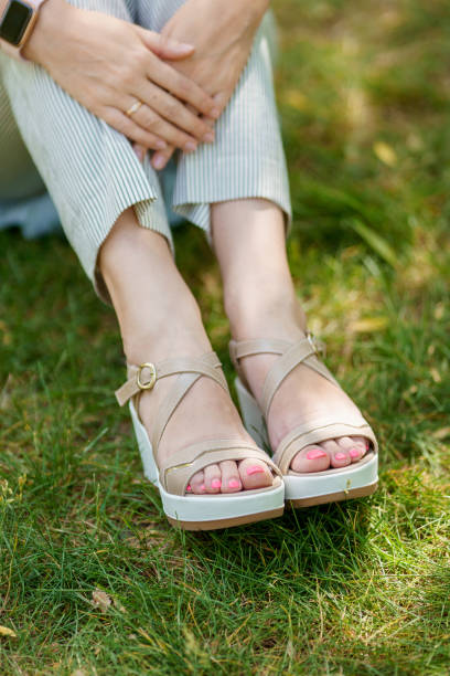 A woman's feet in summer shoes and stripped pants standing on the green grass stock photo