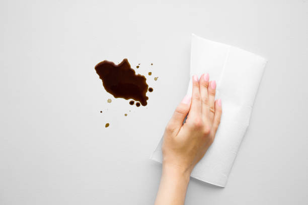 Woman's hand cleaning fresh spilled dark beverage from gray desk. Coffee stain simple removing with white paper napkin. Cleanup. Close up. Top view. Woman's hand cleaning fresh spilled dark beverage from gray desk. Coffee stain simple removing with white paper napkin. Cleanup. Close up. Top view. spilling stock pictures, royalty-free photos & images