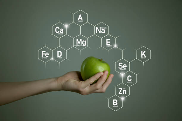 Woman`s hand holding green apple, microelement icons in molecular hexagons on grey background. stock photo