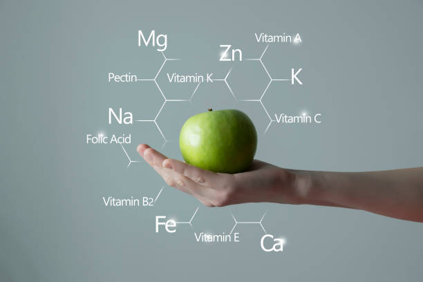 Woman`s hand holding green apple, molecular structure with vitamins and microelelements on background. stock photo