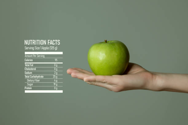 Woman`s hand holding green apple, nutrition facts on grey background. stock photo