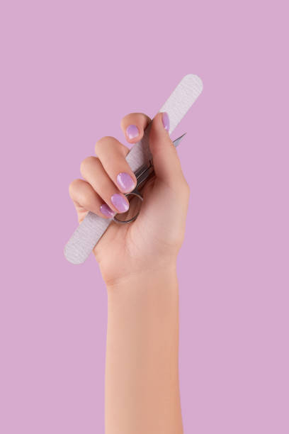 Womans hand holding manicure instrument on pastel lavender background stock photo