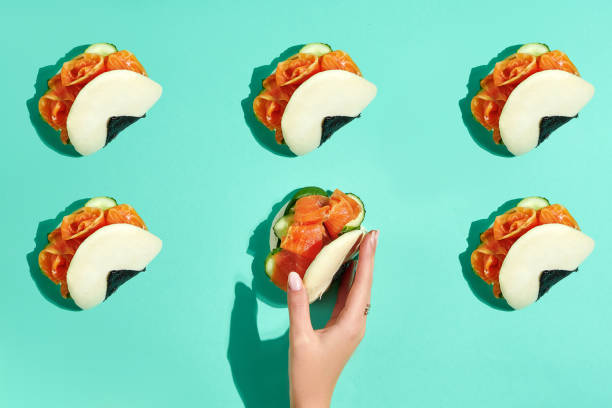 A woman's hand reaches for a bao bun with salmon. Bao buns pattern on turquoise background stock photo