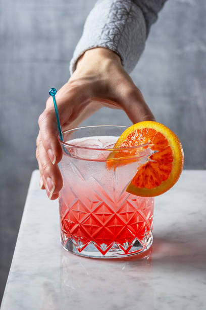 woman's hand reaching for blood orange gin and tonic cocktail on marble counter - blood bar imagens e fotografias de stock