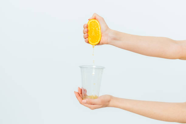 Woman's hand squeezing orange juice from fresh orange stock photo