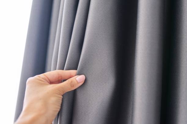 Woman's hand touching curtain, gray blackout fabric, light-blocking fabric stock photo