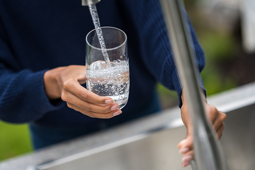 Close-up of woman's hands filling glass with water in garden sink.