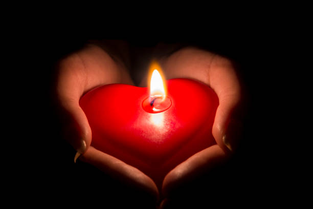 mani della donna che tengono una candela a forma di cuore al buio - san valentino single foto e immagini stock