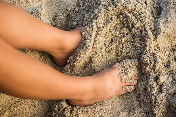 Woman's legs in the sand A tan woman's legs in wet sand human feet buried in sand. summer beach stock pictures, royalty-free photos & images