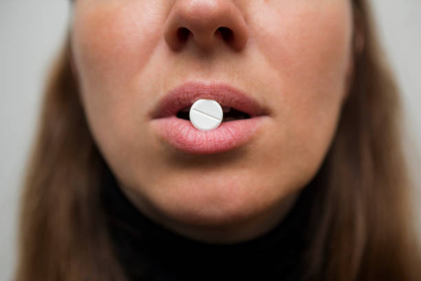 Womans lips hold a large white round pill. Healthcare concept with medicines. Woman taking a tablet from headache or painkiller or abortion pill. Shallow depth of field. Womans lips hold a large white round pill. Healthcare concept with medicines. Woman taking a tablet from headache or painkiller or abortion pill. Shallow depth of field. abortion pill stock pictures, royalty-free photos & images