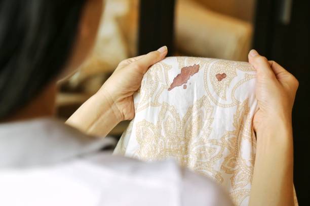 Women hold bed sheet with period blood spot stains on blur background. Need to be cleaning. Women hold bed sheet with period blood spot stains on blur background. Need to be cleaning. woman bleeding stock pictures, royalty-free photos & images