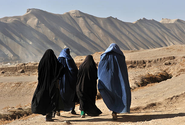 Women in burqa, Afghanistan Bamyian city, Bamyian Province, Afghanistan - November 14, 2010: Four Afghan women in blue and black burqa walking on dirt path in barren land afghanistan stock pictures, royalty-free photos & images