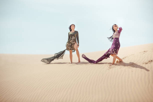 Women in desert landscape. Travel concept Two arabian women in national clothes travelling in desert. Copy space landscape of sand dunes and blue sky. Creative art fashion shot travel concept. hot arabic girl stock pictures, royalty-free photos & images